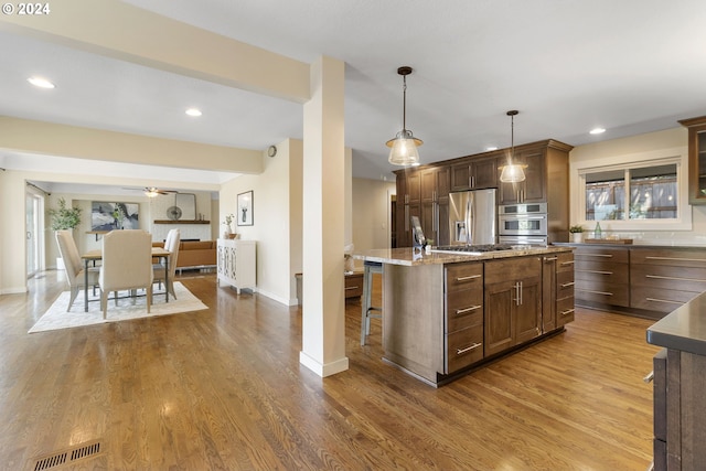 kitchen featuring ceiling fan, stainless steel appliances, pendant lighting, a breakfast bar area, and a kitchen island with sink