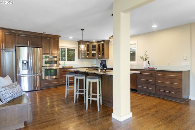 kitchen with light stone countertops, dark hardwood / wood-style flooring, stainless steel appliances, and hanging light fixtures