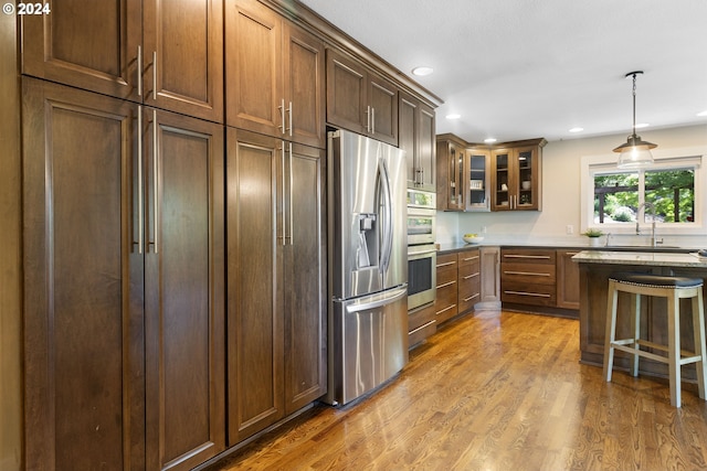 kitchen with stainless steel fridge, sink, pendant lighting, light hardwood / wood-style floors, and a breakfast bar area