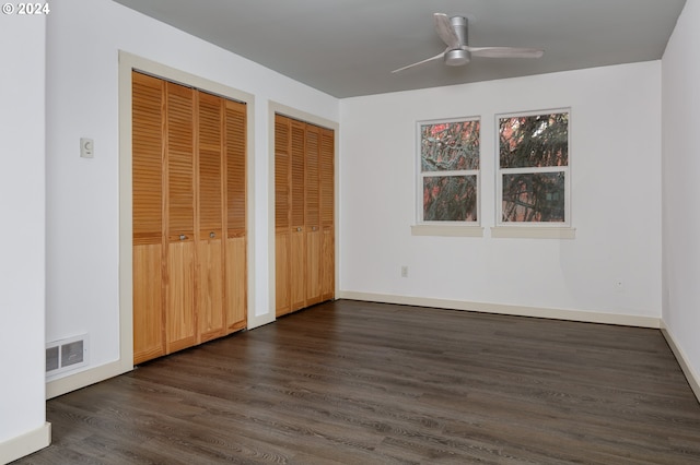 unfurnished bedroom featuring ceiling fan, dark hardwood / wood-style flooring, and two closets