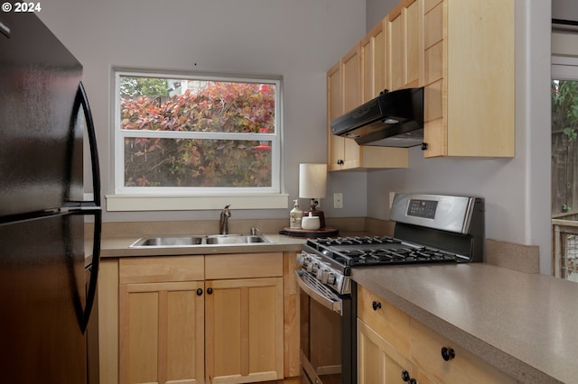 kitchen featuring gas range, black fridge, light brown cabinetry, and sink