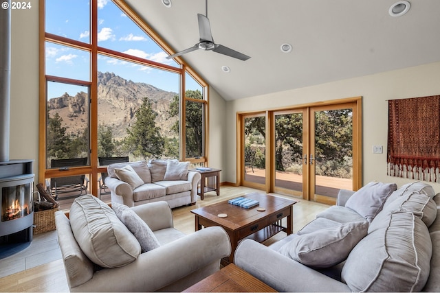 living room with a wood stove, ceiling fan, high vaulted ceiling, a mountain view, and light hardwood / wood-style floors