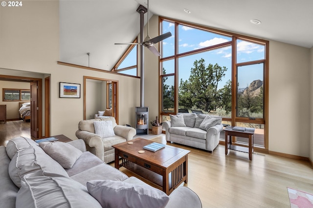 living room with light wood-type flooring, expansive windows, ceiling fan, high vaulted ceiling, and a wood stove