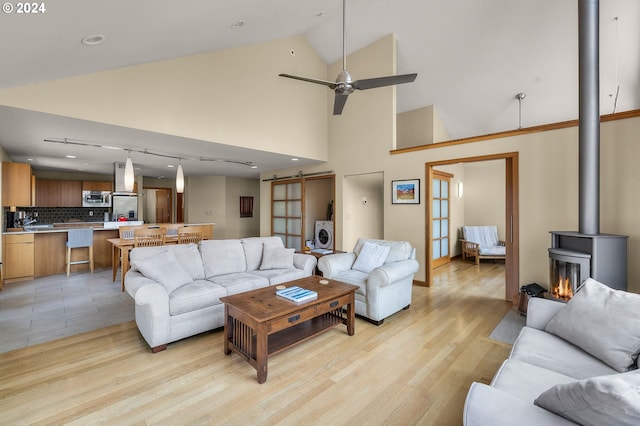 living area with a barn door, a wood stove, a ceiling fan, and light wood-style flooring