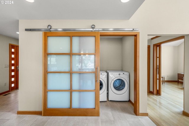 laundry area featuring a barn door, washer and clothes dryer, and light hardwood / wood-style floors