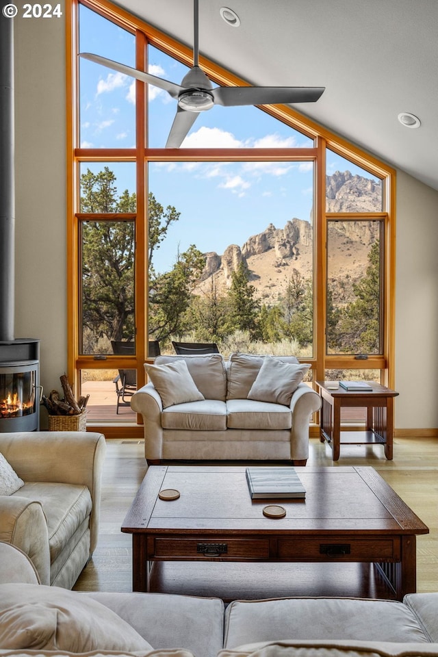 sunroom / solarium with a mountain view, ceiling fan, lofted ceiling, and a wood stove