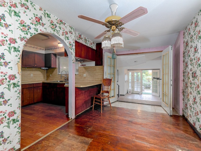 kitchen with wallpapered walls, dark wood finished floors, backsplash, light countertops, and a sink