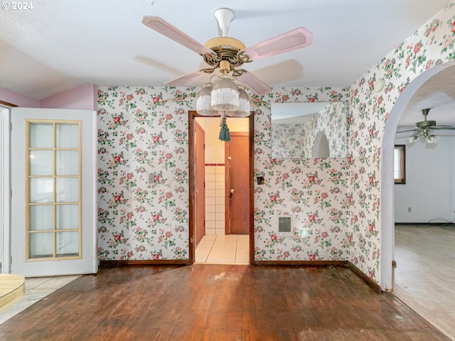 spare room with wallpapered walls, ceiling fan, arched walkways, and wood finished floors