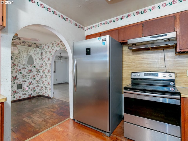 kitchen featuring arched walkways, ceiling fan, under cabinet range hood, light countertops, and appliances with stainless steel finishes