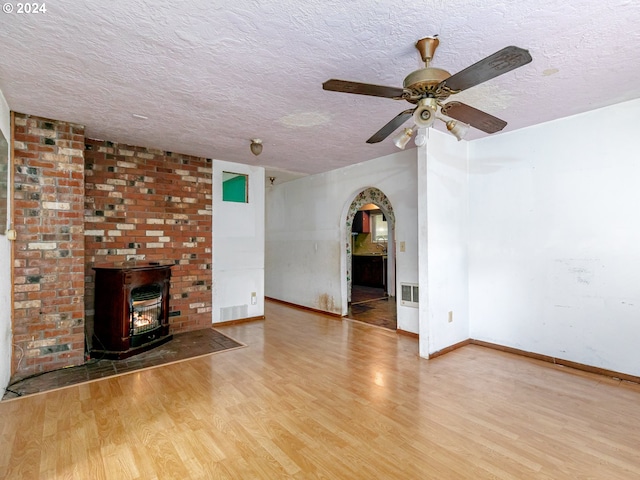 unfurnished living room with arched walkways, visible vents, a wood stove, a textured ceiling, and wood finished floors