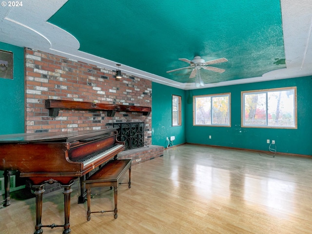 sitting room featuring ceiling fan, a textured ceiling, a fireplace, baseboards, and light wood-type flooring