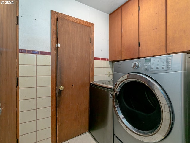 clothes washing area featuring a wainscoted wall, cabinet space, tile walls, and light tile patterned floors