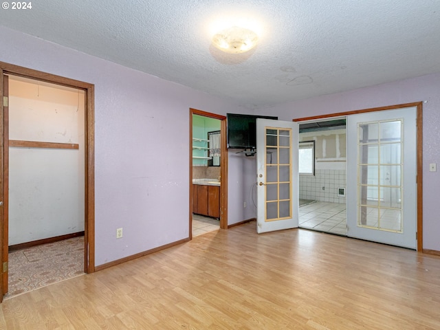 unfurnished bedroom with light wood-style floors, ensuite bath, a textured ceiling, and french doors