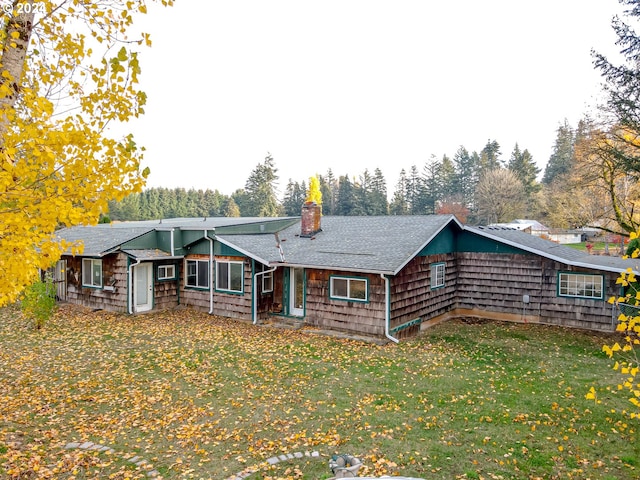 view of front of home with a shingled roof, a chimney, and a front yard