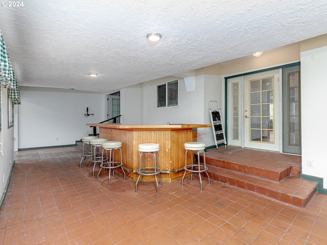 bar featuring baseboards, a textured ceiling, and a bar