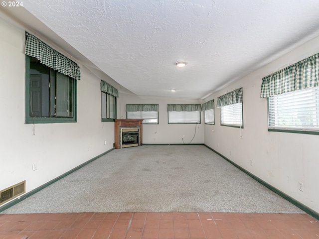 unfurnished living room featuring carpet flooring, visible vents, baseboards, and a textured ceiling