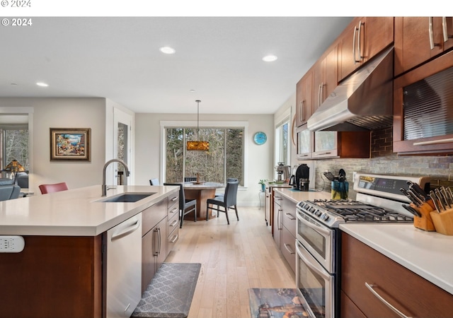 kitchen with sink, pendant lighting, backsplash, stainless steel appliances, and a center island with sink