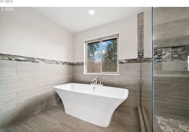 bathroom with a tub to relax in, tile patterned flooring, and tile walls