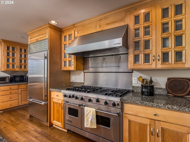 kitchen with dark stone countertops, premium appliances, extractor fan, and dark wood-type flooring