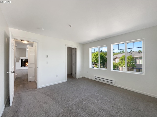 unfurnished bedroom featuring a walk in closet, a baseboard radiator, dark colored carpet, and a closet