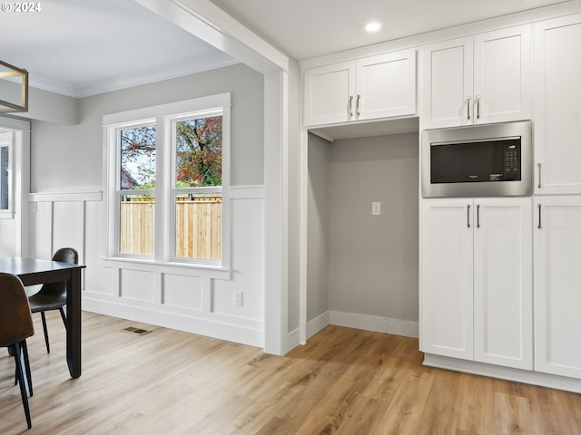 kitchen with light hardwood / wood-style flooring, ornamental molding, stainless steel microwave, and white cabinets