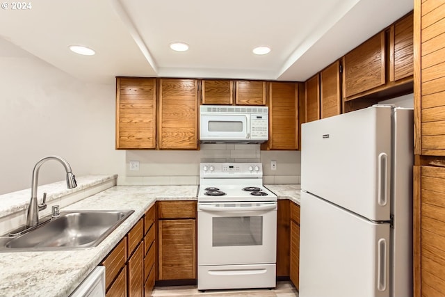 kitchen featuring brown cabinets, recessed lighting, light countertops, a sink, and white appliances