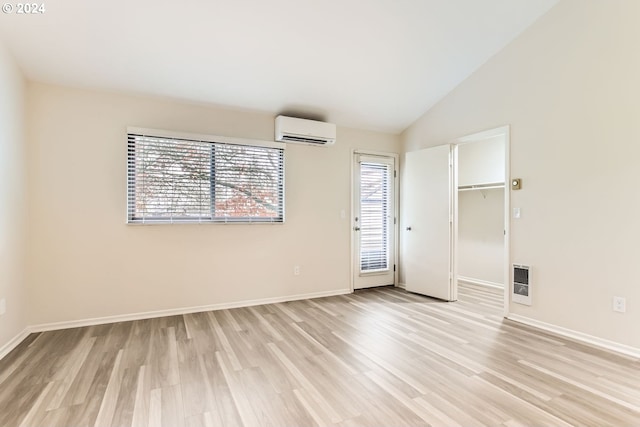 unfurnished room featuring lofted ceiling, light wood-style flooring, baseboards, an AC wall unit, and heating unit