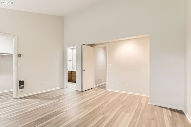 interior space with light wood-type flooring, baseboards, a high ceiling, and heating unit