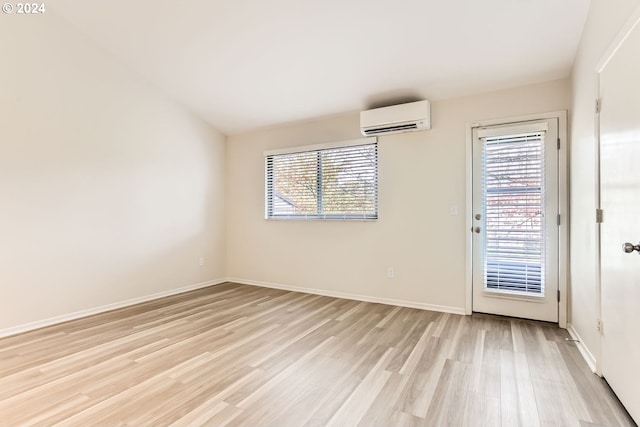 unfurnished room featuring light wood-type flooring, a wealth of natural light, a wall unit AC, and baseboards