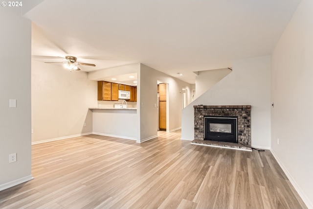 unfurnished living room featuring ceiling fan, light wood finished floors, a glass covered fireplace, and baseboards