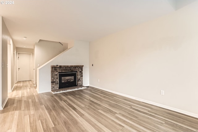 unfurnished living room with a brick fireplace, baseboards, and wood finished floors