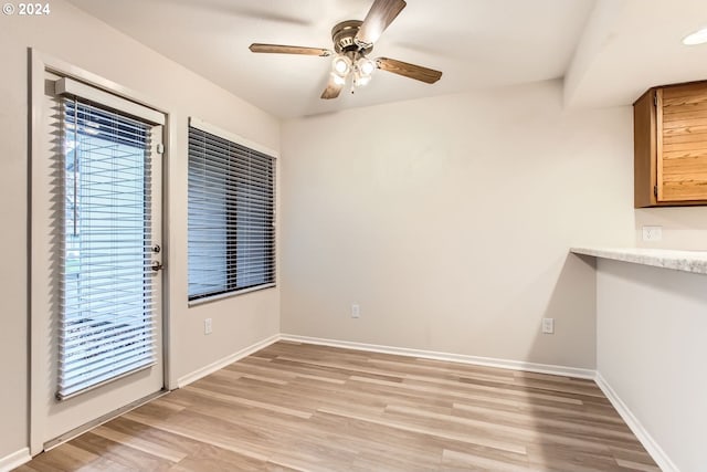 unfurnished dining area with light wood-style floors, plenty of natural light, ceiling fan, and baseboards