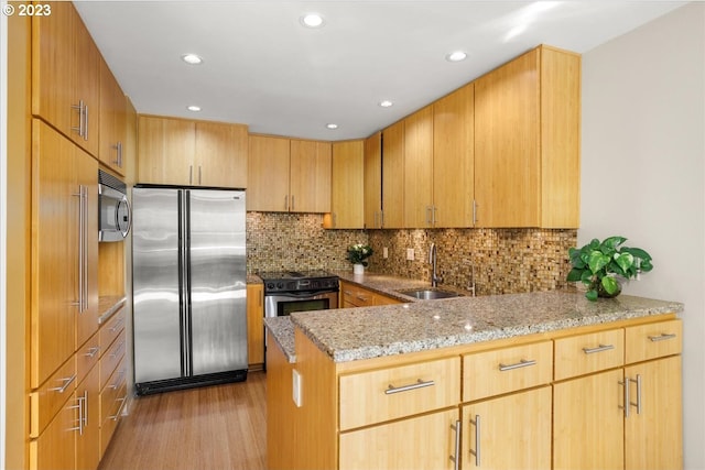 kitchen featuring light stone counters, light wood-type flooring, appliances with stainless steel finishes, sink, and kitchen peninsula