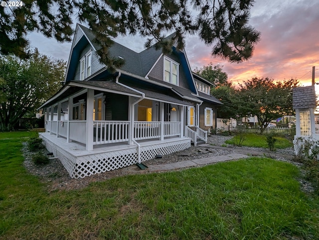 back house at dusk with a lawn and a porch