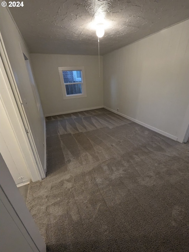 spare room with a textured ceiling and dark carpet