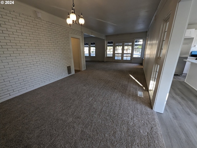 spare room featuring a chandelier, wood-type flooring, ornamental molding, and brick wall