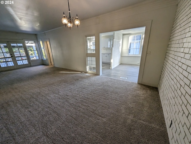 carpeted empty room featuring a notable chandelier, ornamental molding, and french doors