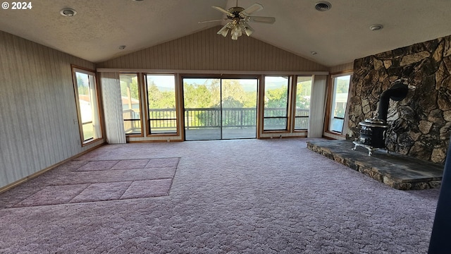 unfurnished living room featuring a healthy amount of sunlight, carpet, a textured ceiling, and a wood stove