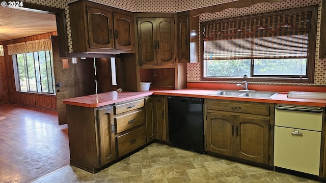 kitchen featuring wood walls, sink, kitchen peninsula, dark brown cabinets, and black dishwasher