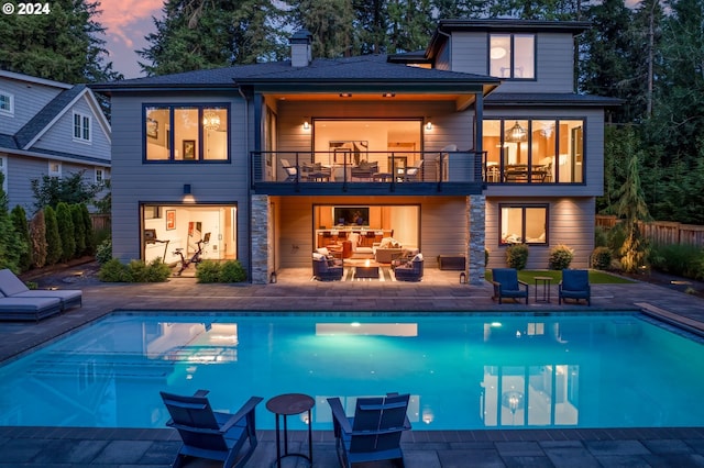 back house at dusk featuring a patio, an outdoor hangout area, and a balcony