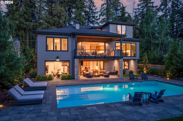 back house at dusk featuring a patio area, a fenced in pool, and a balcony