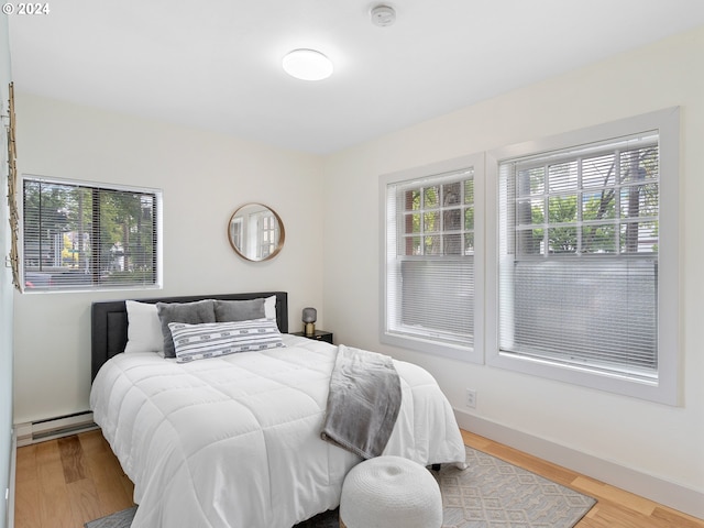 bedroom featuring multiple windows, baseboards, baseboard heating, and wood finished floors