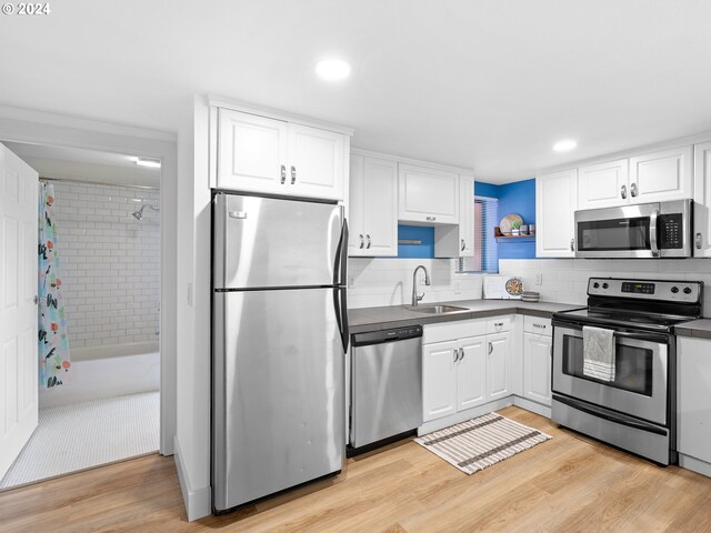 kitchen featuring light wood-type flooring, stainless steel appliances, sink, decorative backsplash, and white cabinets