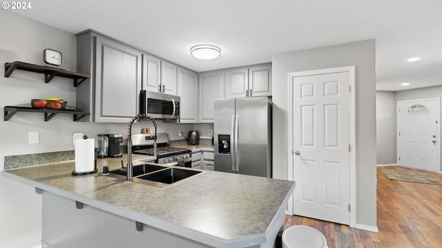 kitchen with gray cabinetry, sink, kitchen peninsula, wood-type flooring, and stainless steel appliances