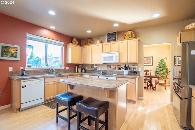 kitchen featuring light brown cabinets, white appliances, a center island, a breakfast bar area, and light wood-type flooring