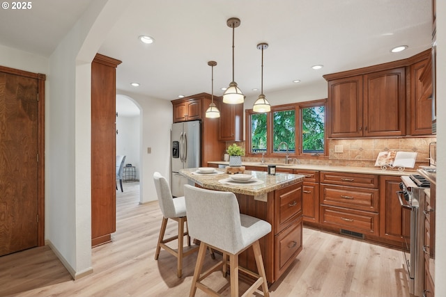 4243 Spring Rock Cir, West Linn, OR 97068 - kitchen featuring arched walkways, appliances with stainless steel finishes, light wood finished floors, a kitchen bar, and backsplash