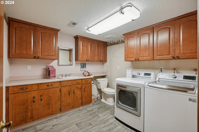 laundry area featuring light wood-type flooring, sink, a textured ceiling, and washer and clothes dryer