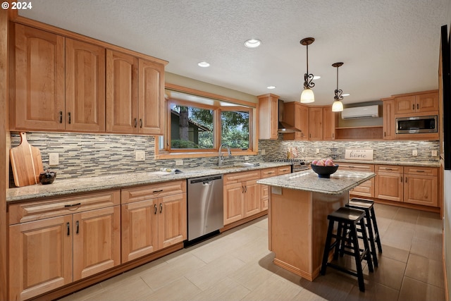 kitchen with light stone counters, decorative light fixtures, a wall mounted AC, appliances with stainless steel finishes, and a kitchen island