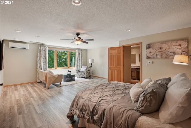 bedroom featuring ceiling fan, ensuite bathroom, a textured ceiling, an AC wall unit, and light wood-type flooring