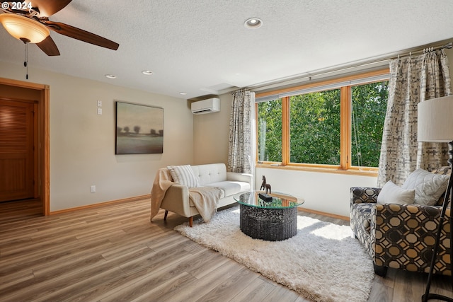 living room featuring wood-type flooring, ceiling fan, a textured ceiling, and a wall unit AC